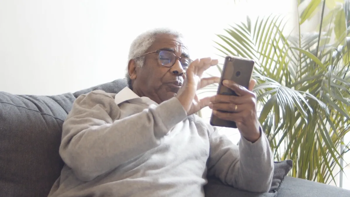 An elderly man at home, smiling at a video call with his family