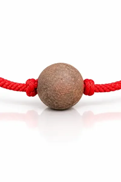 Close-up of the brown NavaPashanam Gutika bead with red thread and a glossy white reflection.