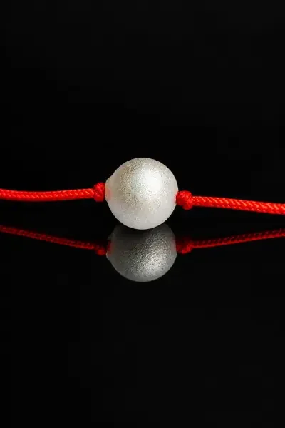 Front-facing close-up of the 10 Gram Parad Gutika attached to a red sacred thread, presented against a glossy black background with a clear reflection.
