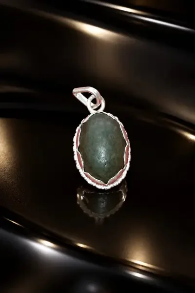 Navapashanam Pendant featuring a dark stone and detailed silver frame, displayed on a glossy black surface.
