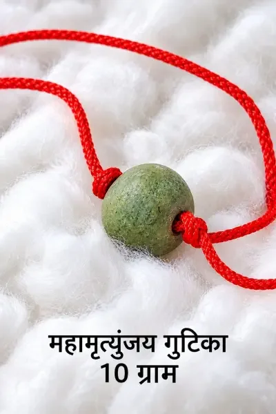Maha - Mrityunjay Gutika 10 Gram with a red sacred thread, placed on soft white fabric, highlighting its green natural texture and round form.