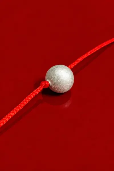10 Gram Parad Gutika displayed on a rich red background with a red sacred thread, highlighting the spherical metallic Parad bead and devotional presentation.