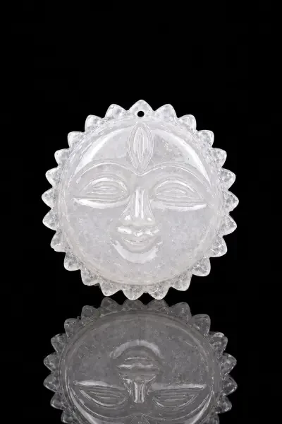 Natural Sphatik Surya Dev idol with a detailed sun face, displayed on a reflective black surface with traditional decor.