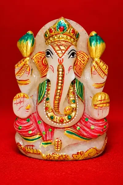 Coloured Sphatik Ganesh Ji idol on a vibrant red background.