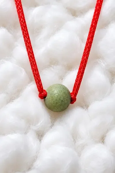Detailed close-up of the Navagraha Gutika placed on soft white fabric, highlighting the green spherical bead, its natural texture and the red sacred thread.