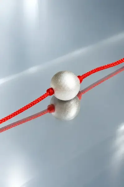 Close-up view of the 10 Gram Parad Gutika on a reflective silver surface, showcasing its smooth metallic finish, detailed texture and red sacred thread.