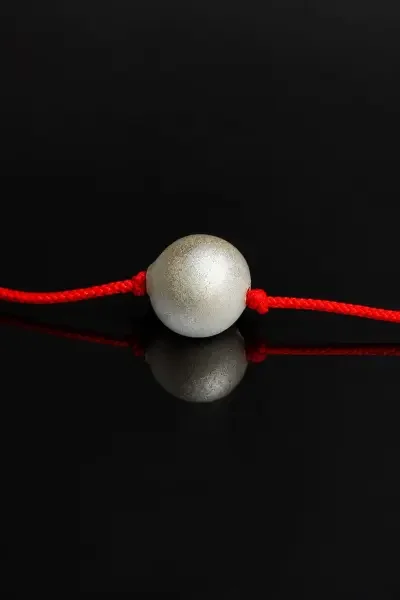Front-facing close-up of the 10 Gram Parad Gutika attached to a red sacred thread, presented against a glossy black background with a clear reflection.