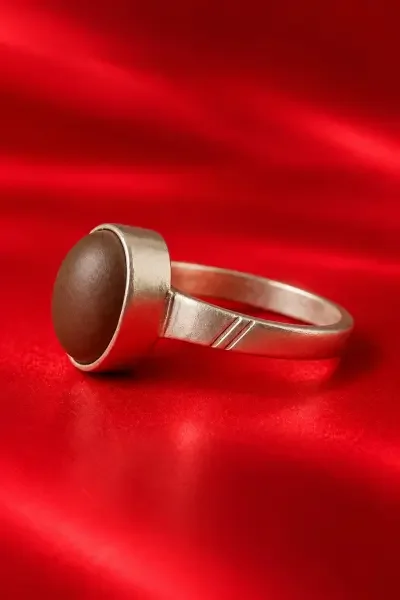 Navapashanam Healing Ring featuring a brown 10g bead in a traditional silver setting, displayed on a luxurious red background.